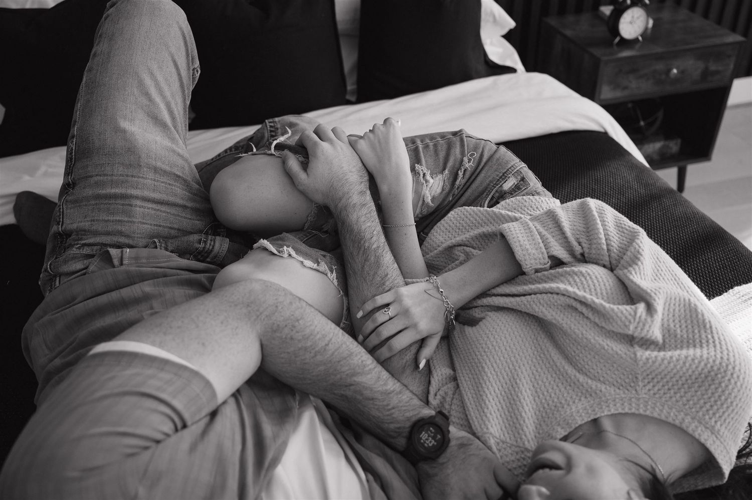 Black and white photo of a couple relaxing together on bedding in casual attire.