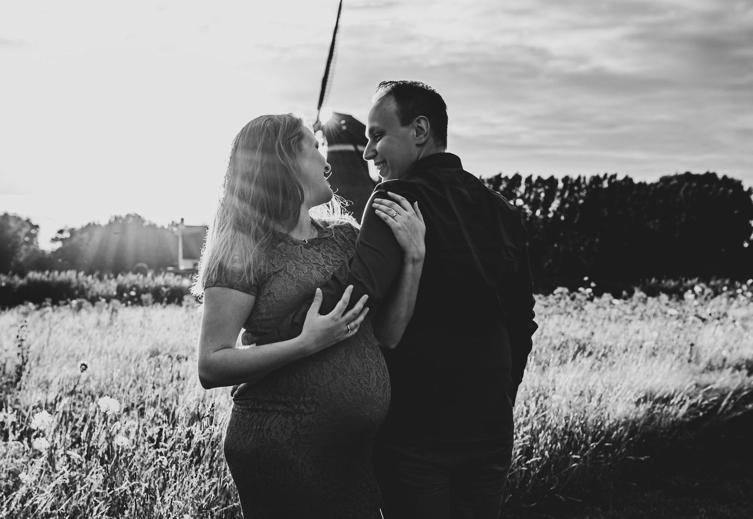 Silhouetted couple embracing in a sunlit field with dramatic sky backdrop.