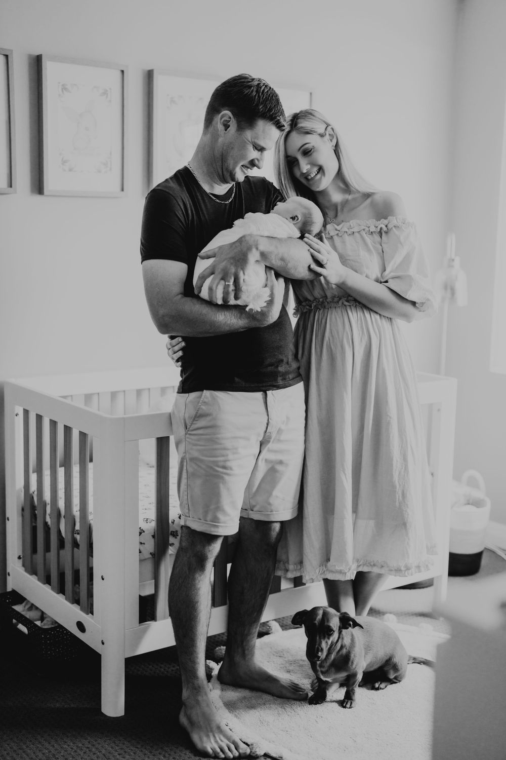 A tender family moment in a nursery with a small dog looking on.