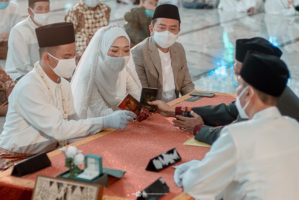 Muslim wedding ceremony with participants in white and masks signing documents.