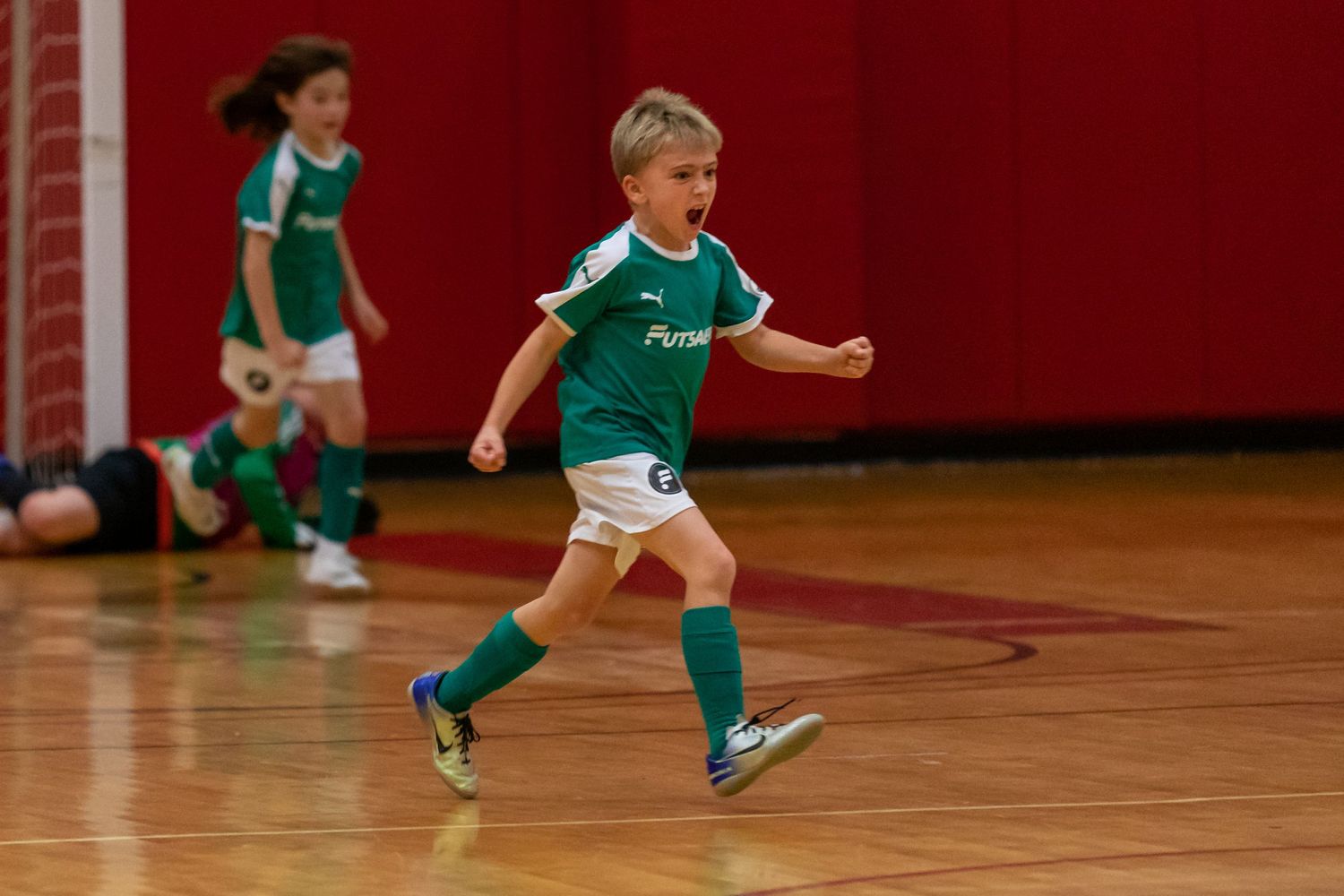 Young players in green uniforms practicing indoor soccer skills.