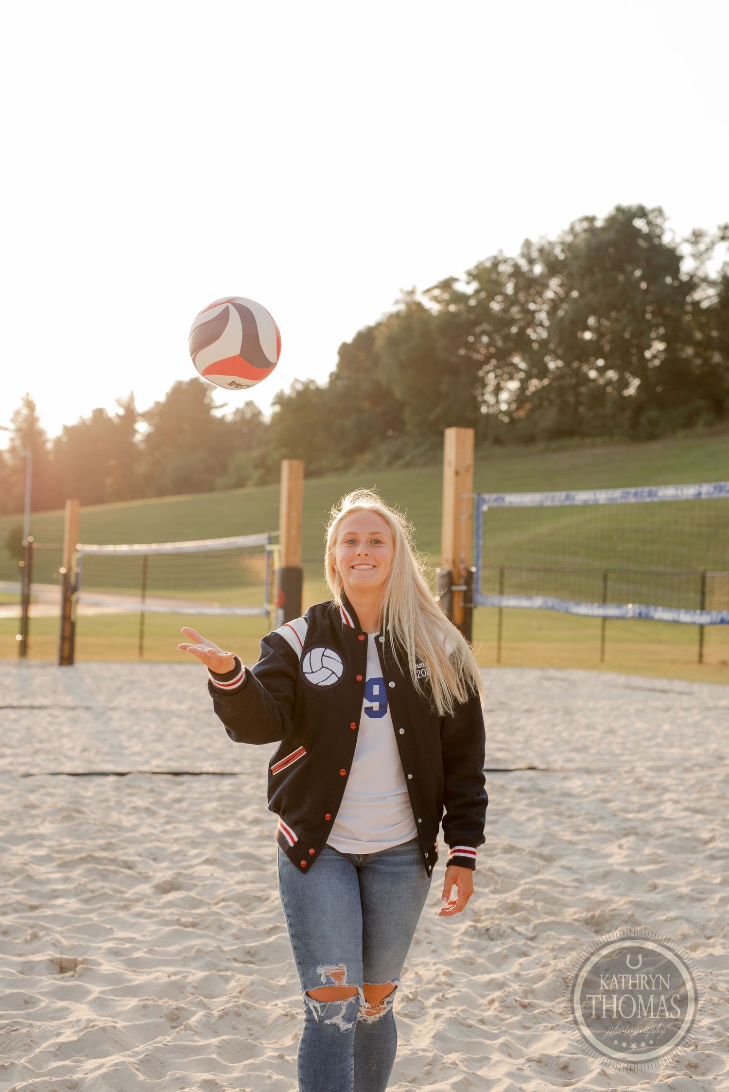 Player tossing volleyball in air on beach court during sunset.