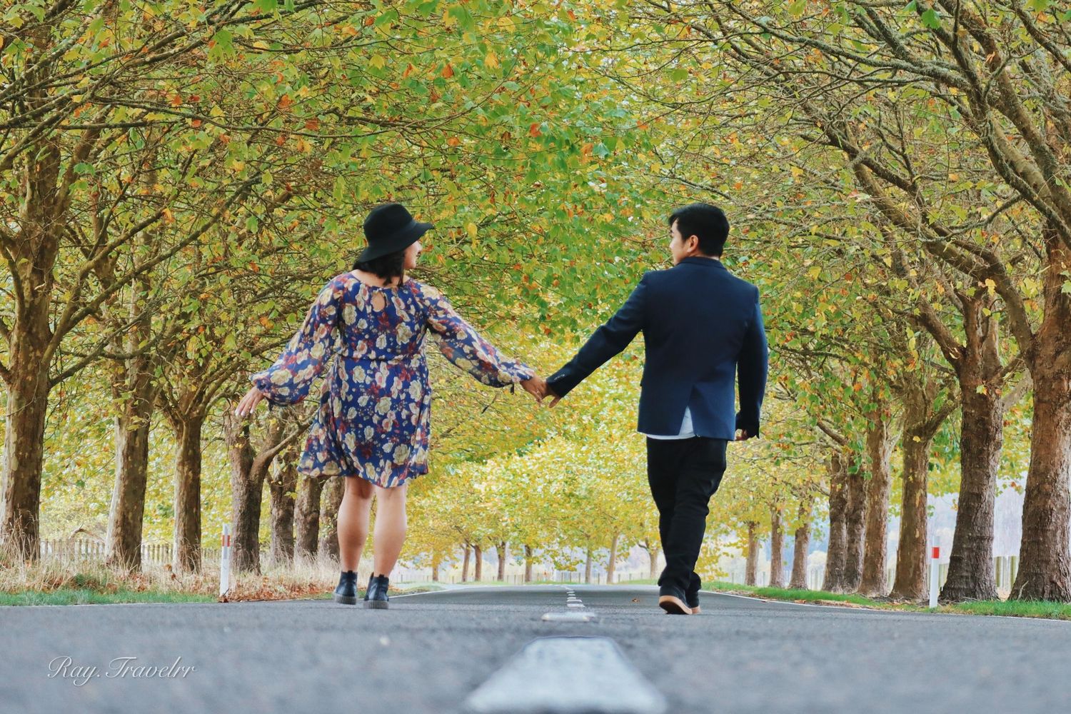 A couple holding hands while walking down a tree-lined path in autumn.