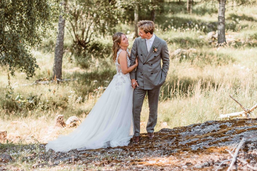 Newlyweds sharing intimate moment on forest path with bride's dress trailing behind.