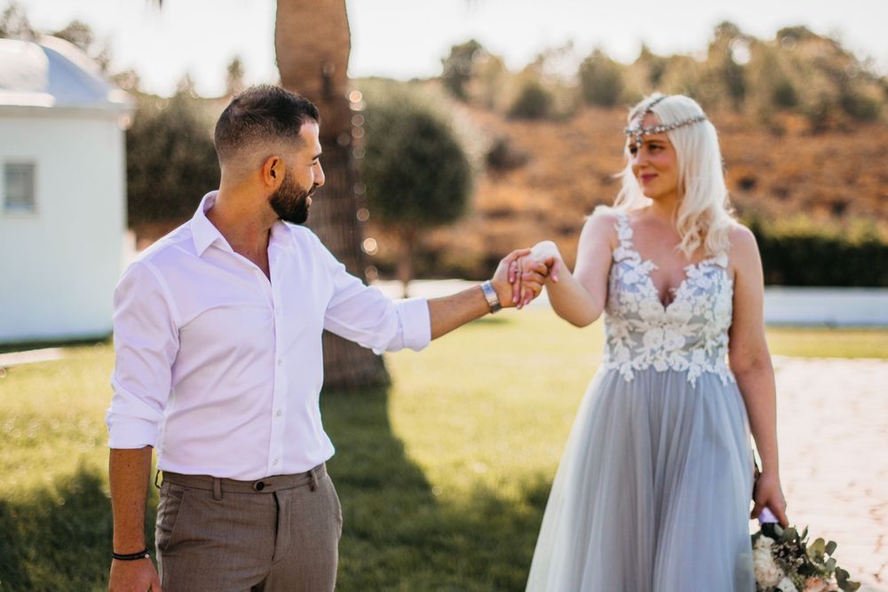 Bride and groom share playful moment on grassy field.