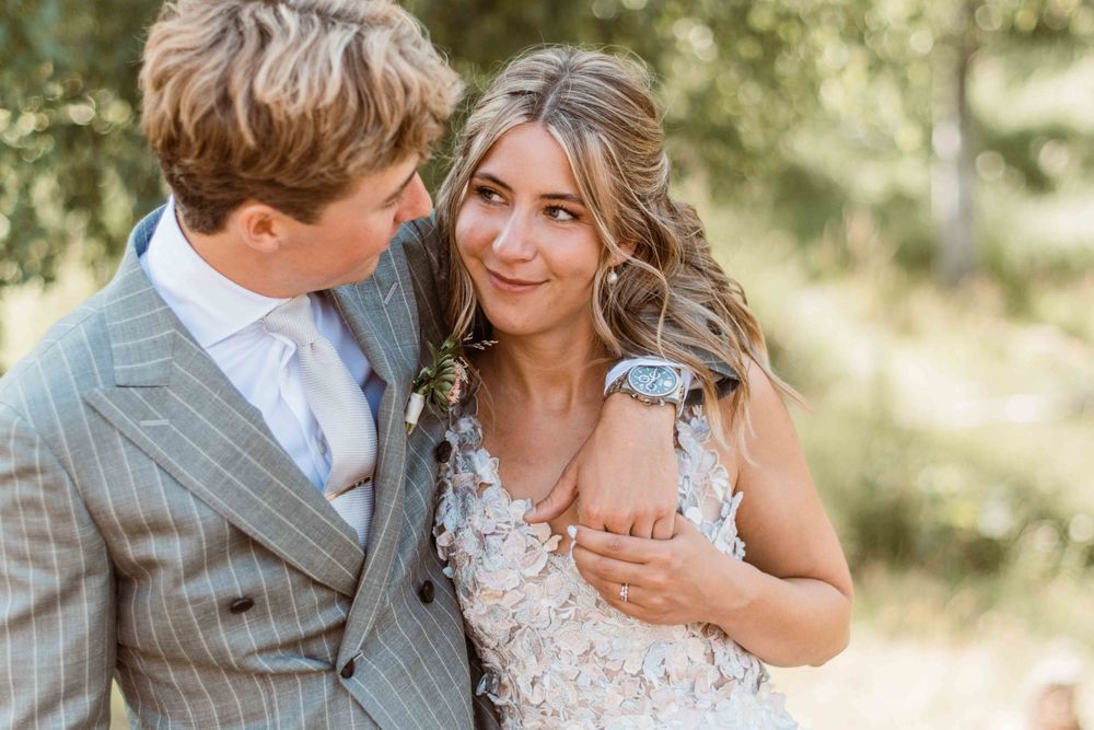 Tender moment between newlyweds in formal attire against natural outdoor backdrop.