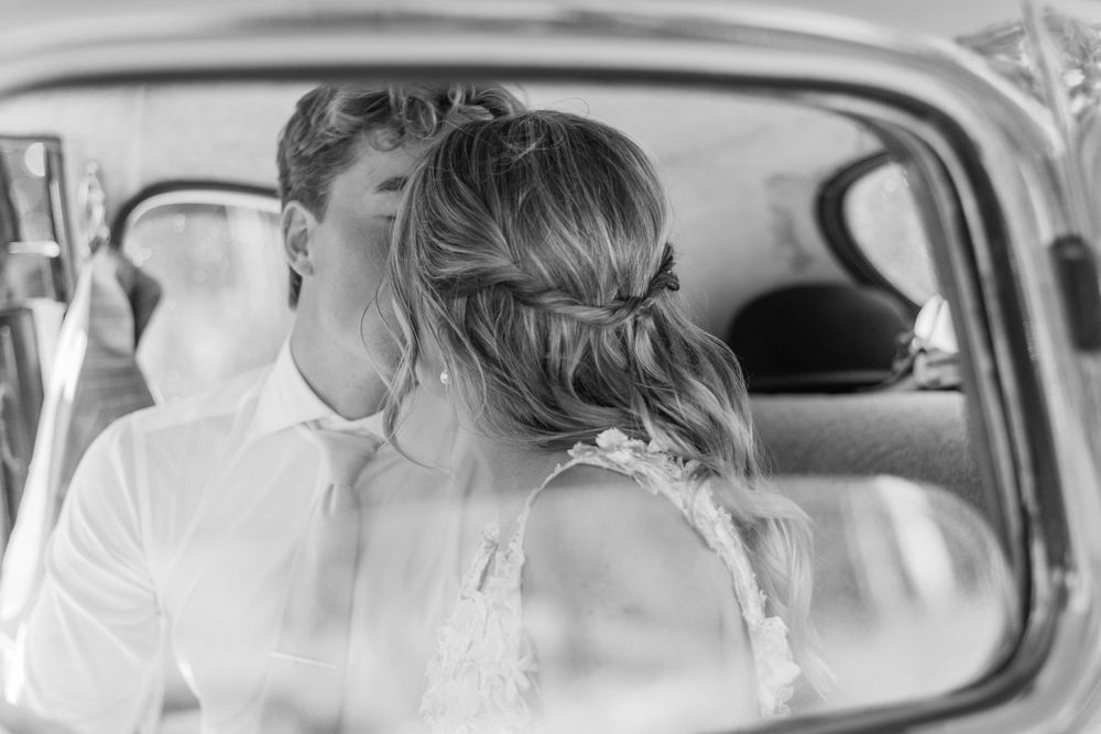 Black and white intimate moment captured inside vintage car after wedding ceremony.