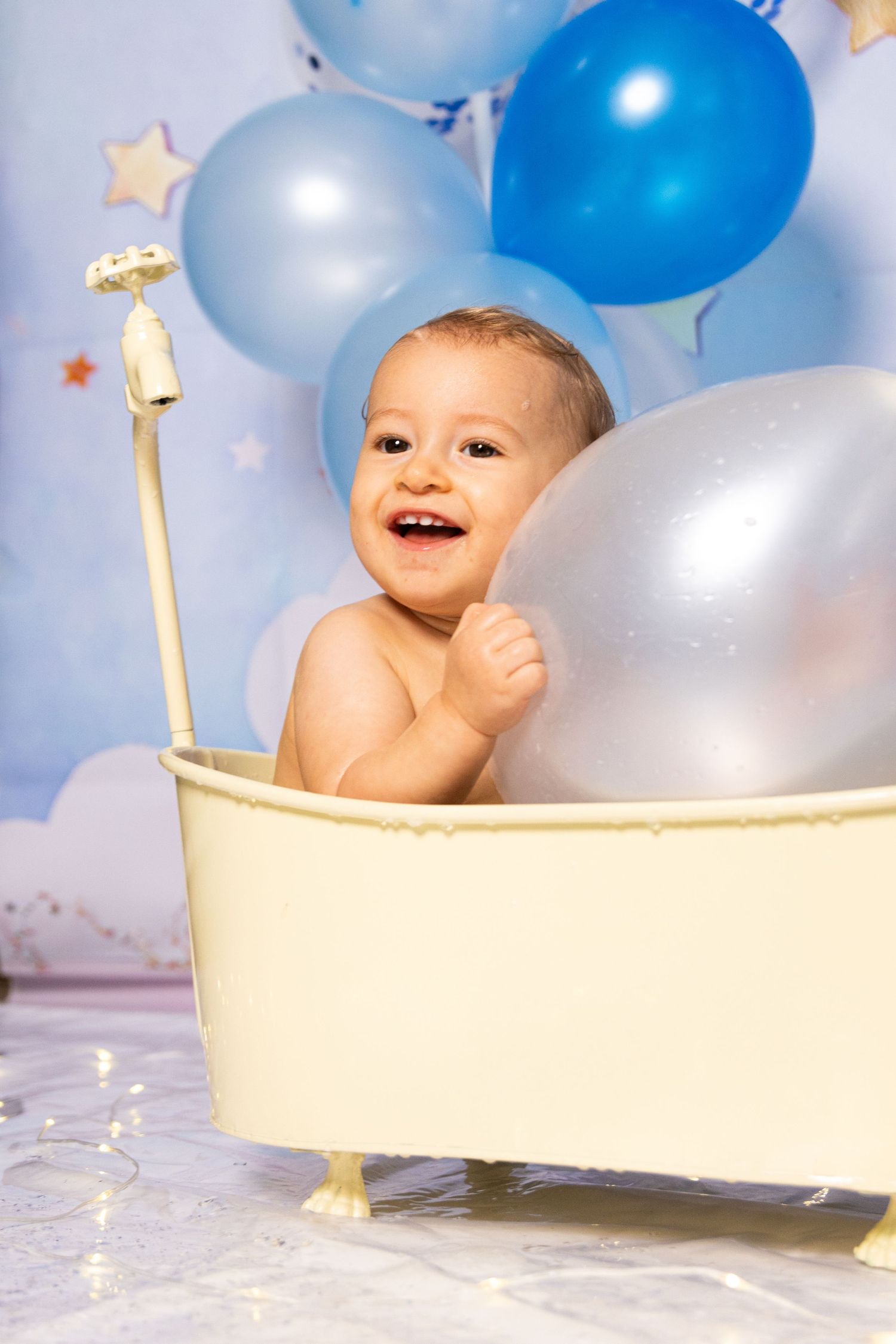 Happy baby in miniature bathtub surrounded by festive blue and white balloons.