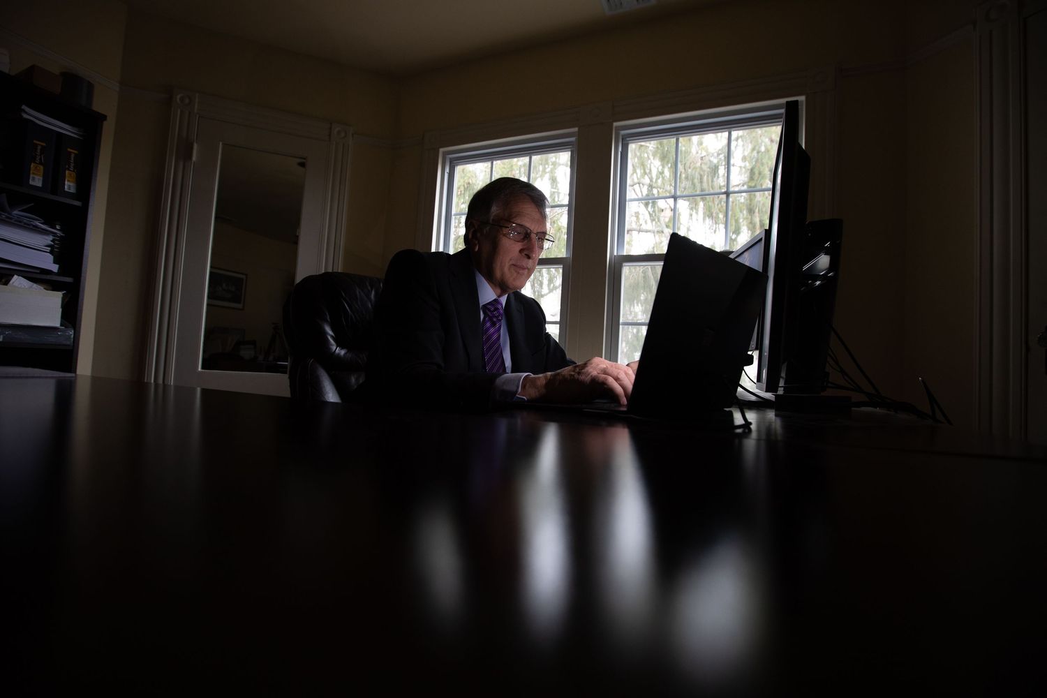 Silhouette of person working at desk with computer in dark room with window light.