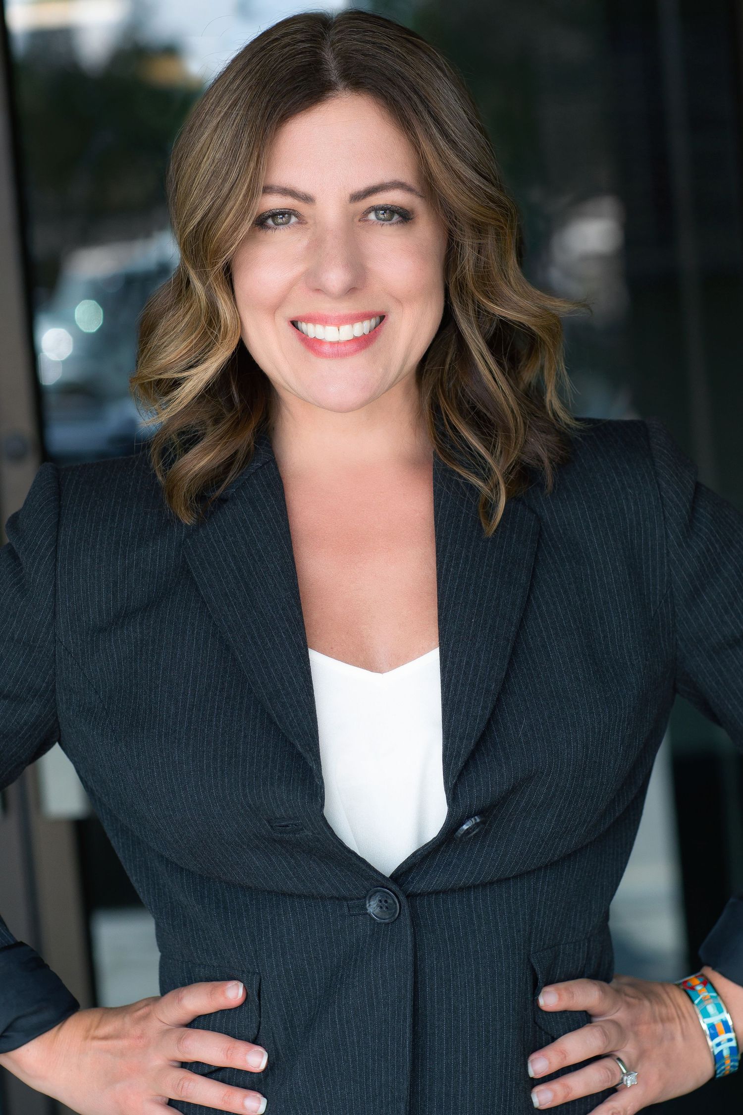 Professional business portrait of person wearing black blazer and white top with wavy hair.
