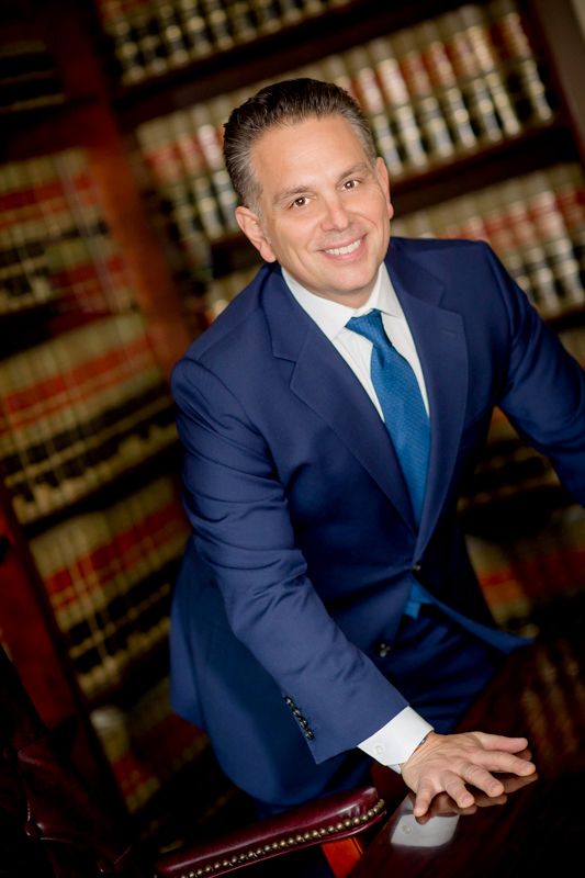 Professional headshot in law office with blue suit and tie against backdrop of law books.