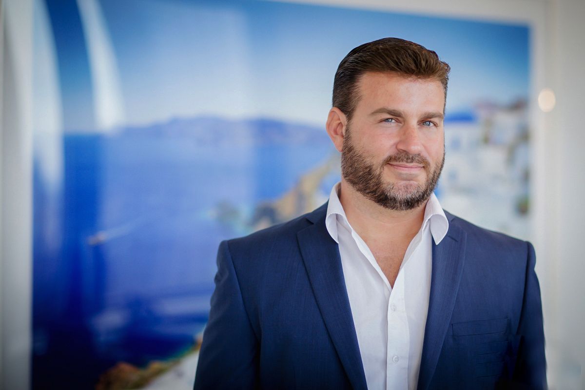 Professional headshot in navy suit with white shirt against blue background.