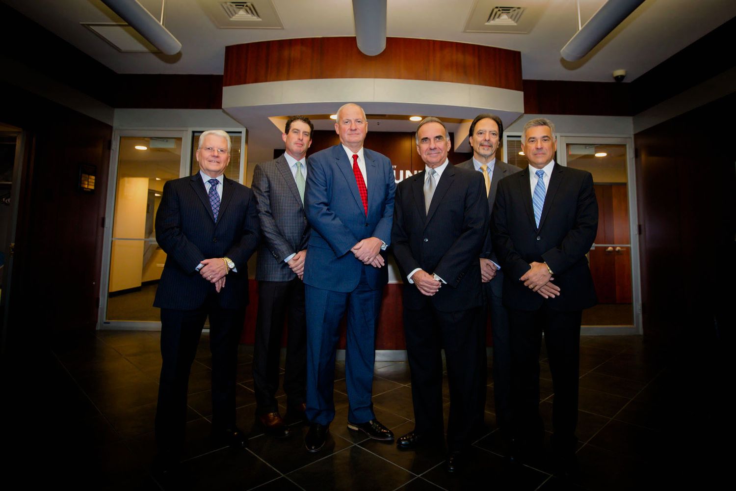 Group of professionals in business suits standing together in office hallway.
