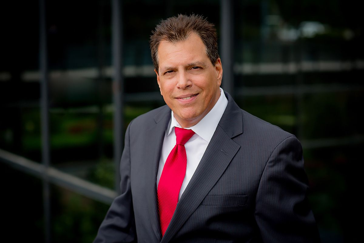 Executive wearing gray suit and bright red tie poses for professional headshot outdoors.