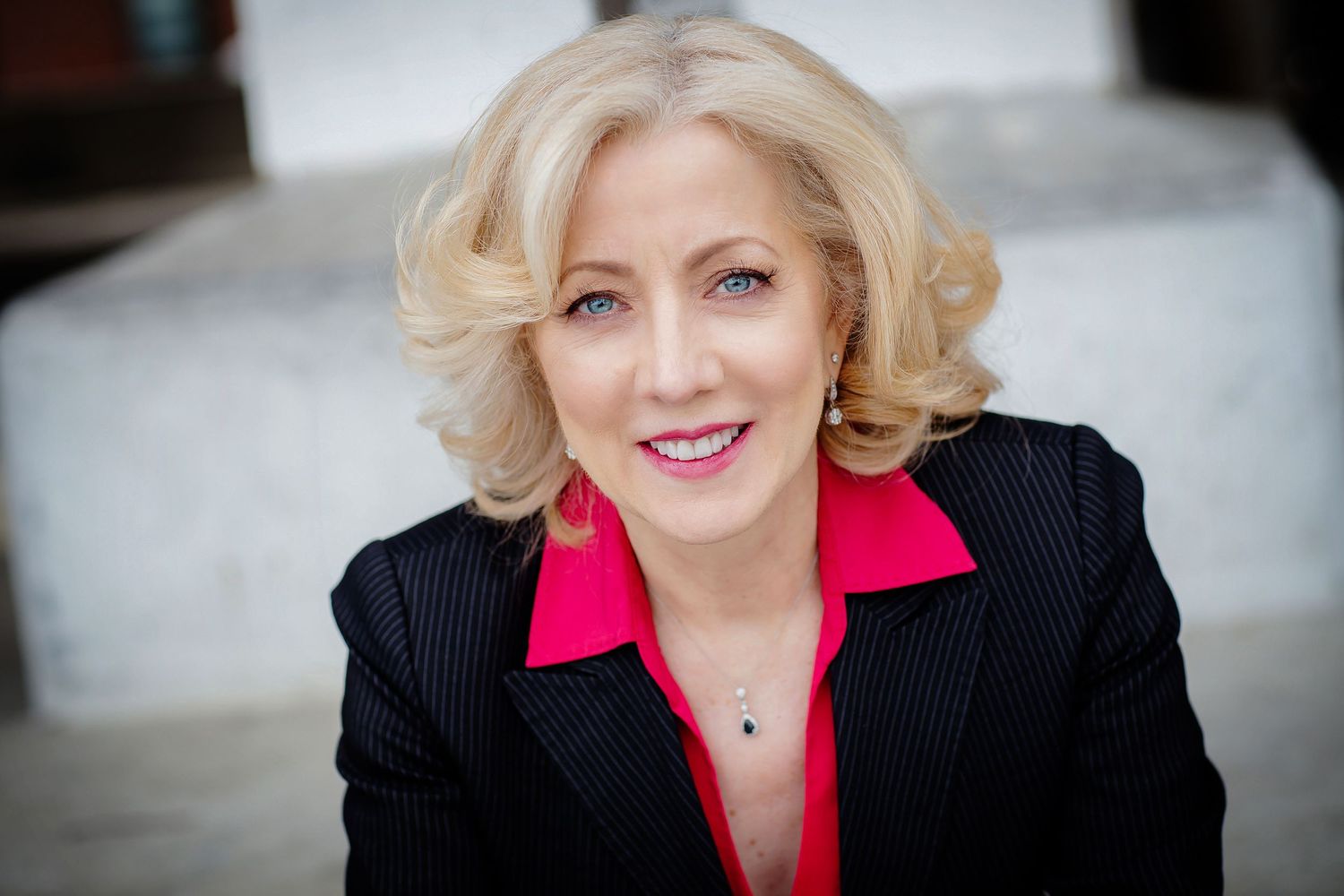 Professional portrait featuring black pinstripe blazer with red collar against light background.