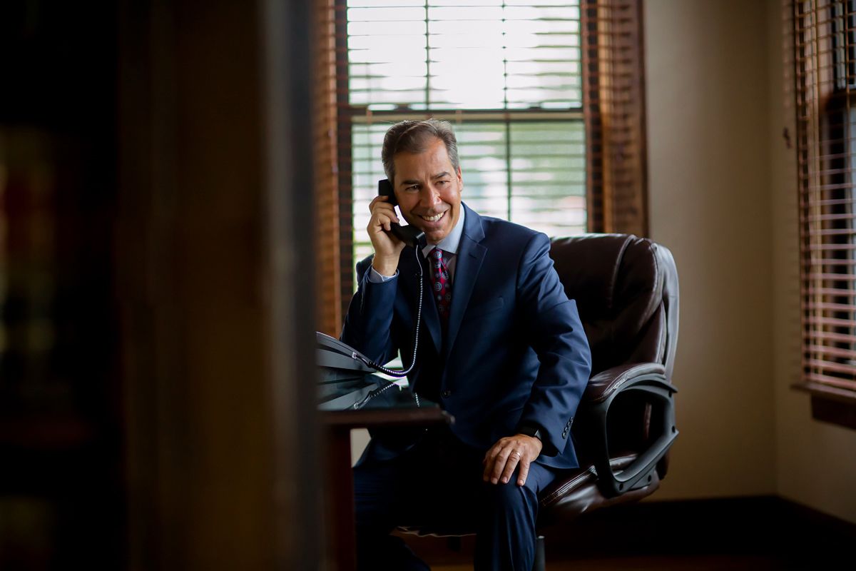 Executive speaking on phone while seated in leather office chair near window.
