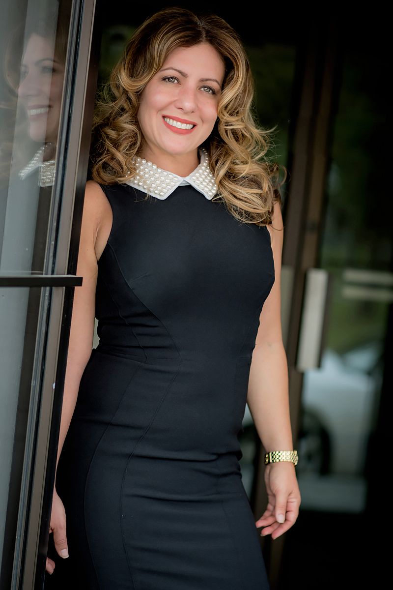 Professional portrait of woman in black dress with white collar leaning against doorframe.