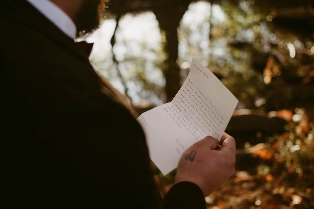 Hands hold handwritten letter in dramatic lighting against forest backdrop.