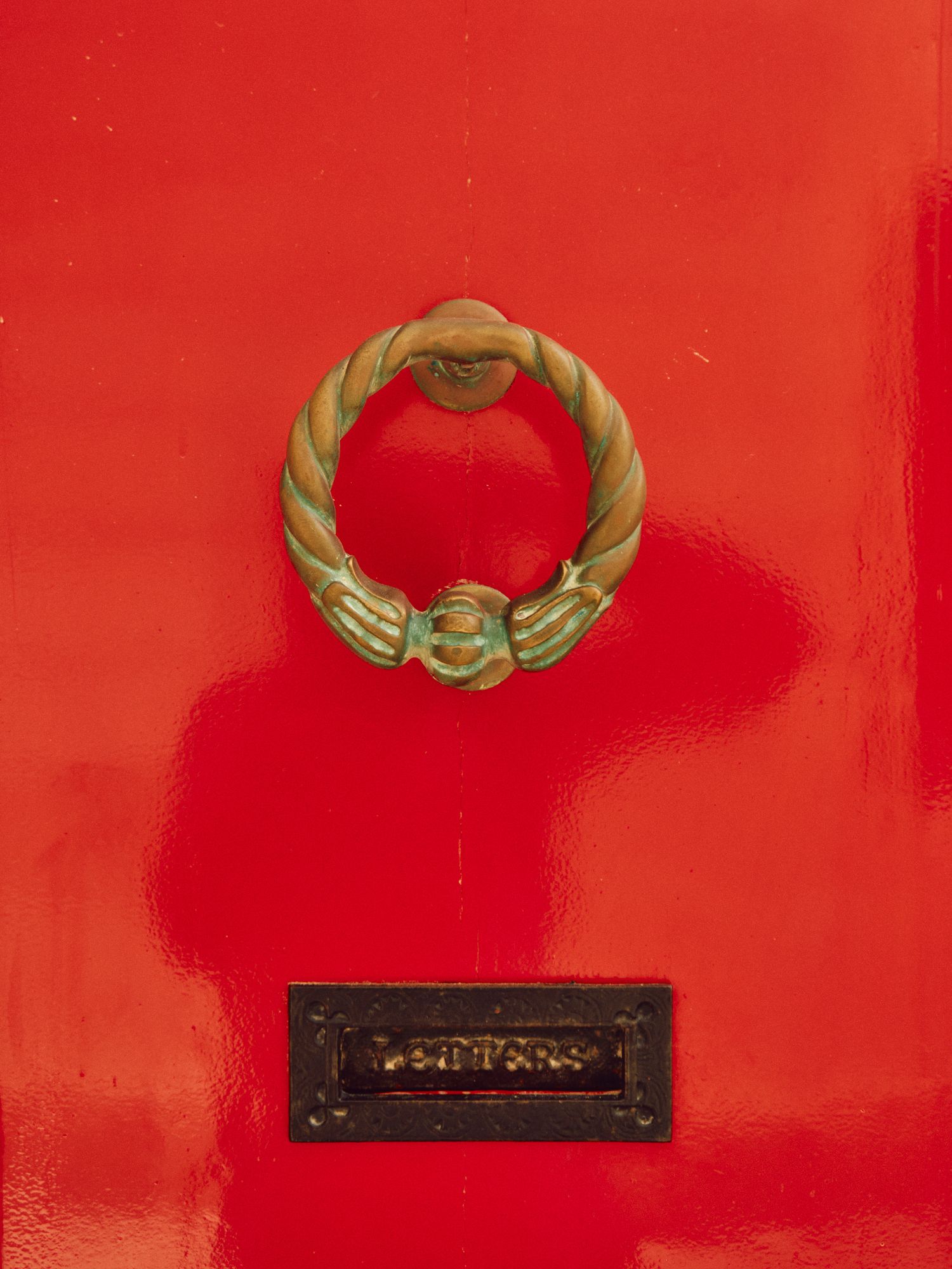 Brass door knocker in circular wreath design mounted on bright red painted door.