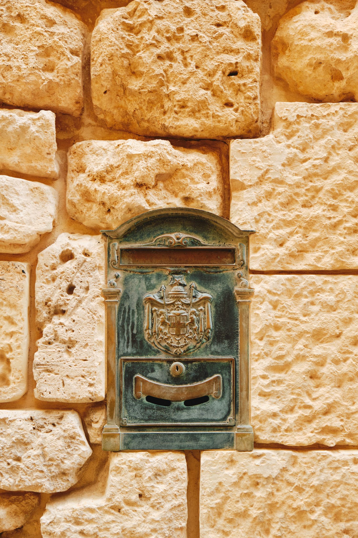 Vintage brass mailbox mounted on textured limestone wall with ornate royal crest design.