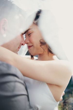 Intimate moment between couple under white veil.