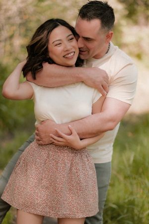 Romantic couple embraces and laughs together in casual outdoor setting.