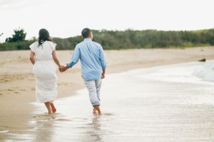 A couple walks barefoot together along the shoreline at the beach.
