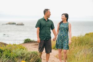 A couple walks hand in hand along a coastal trail on a sunny day.
