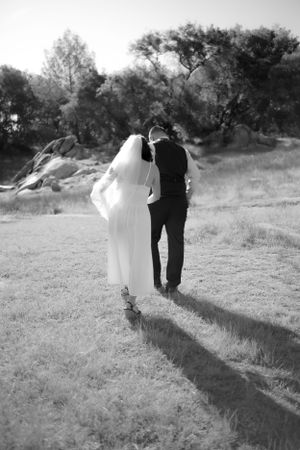 Black and white photo of newlyweds walking together across field.