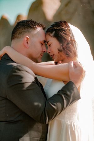Tender moment between couple in wedding attire against sunlit background.