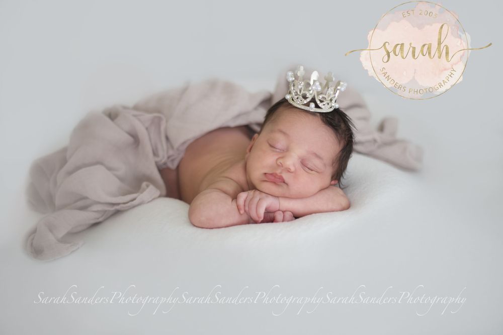 baby sleeping on belly with hands under chin, wearing a tiara