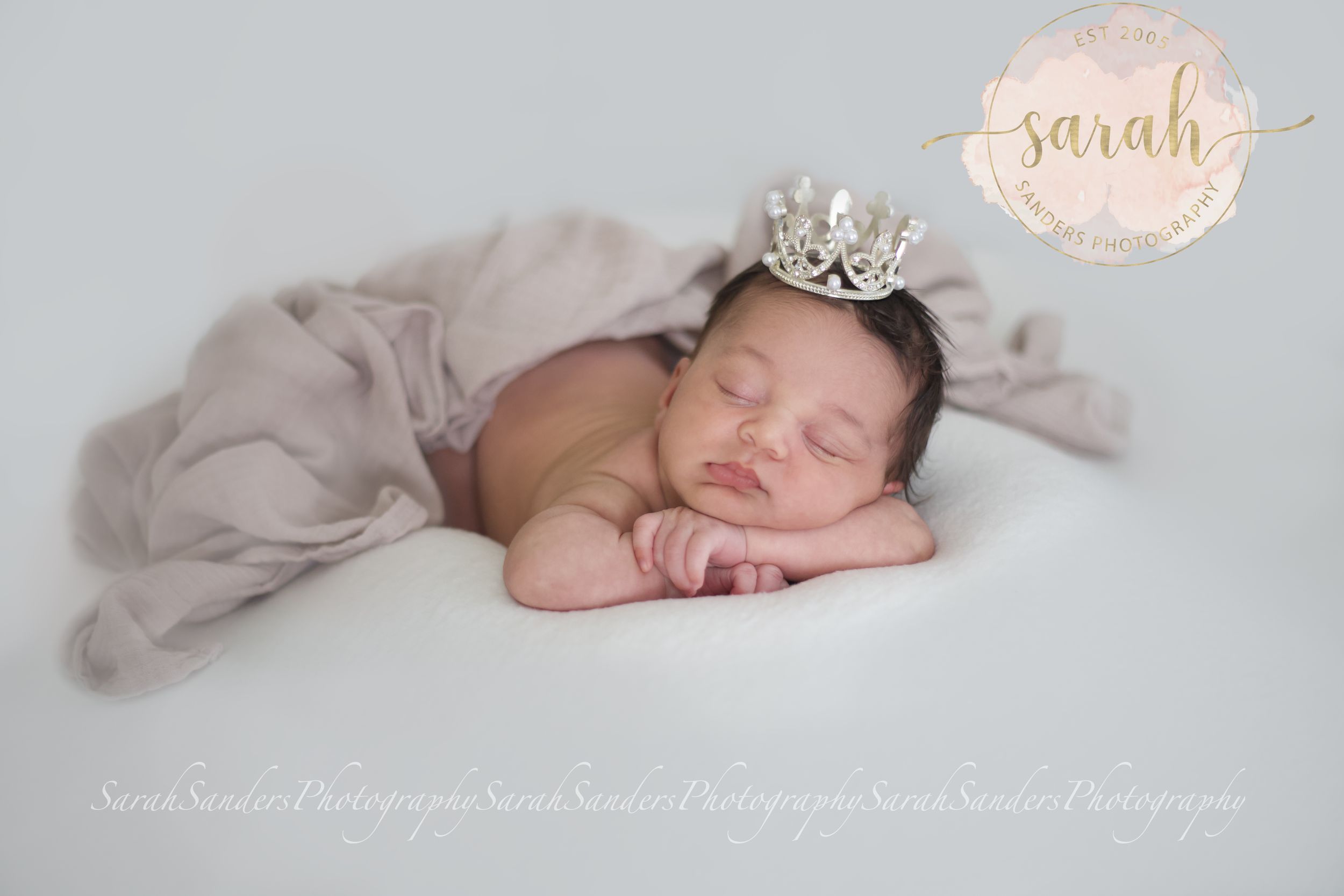 baby sleeping on belly with hands under chin, wearing a tiara