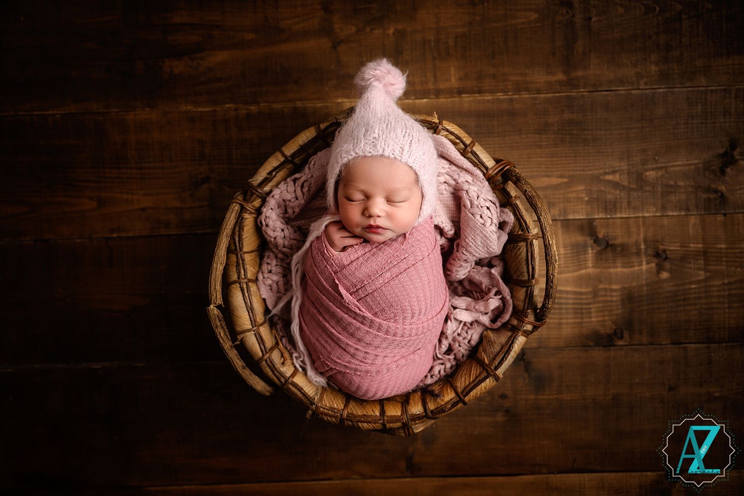 Swaddled infant wearing knit hat rests in rustic wooden basket during photo shoot.