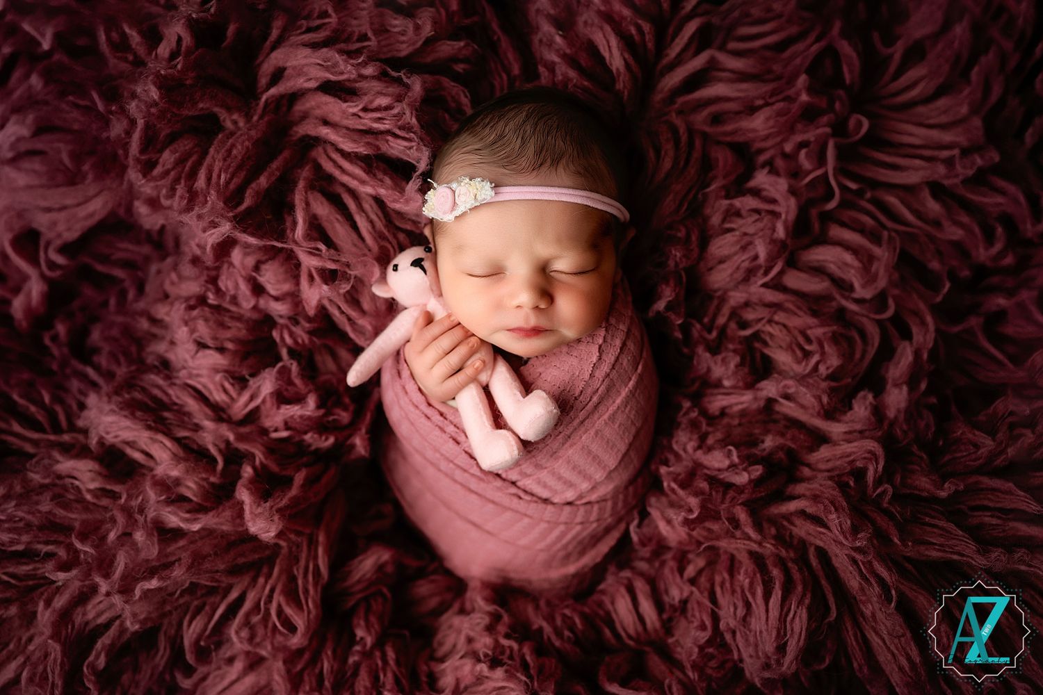 Peaceful newborn swaddled in pink wrap rests on burgundy textured fabric during portrait session.