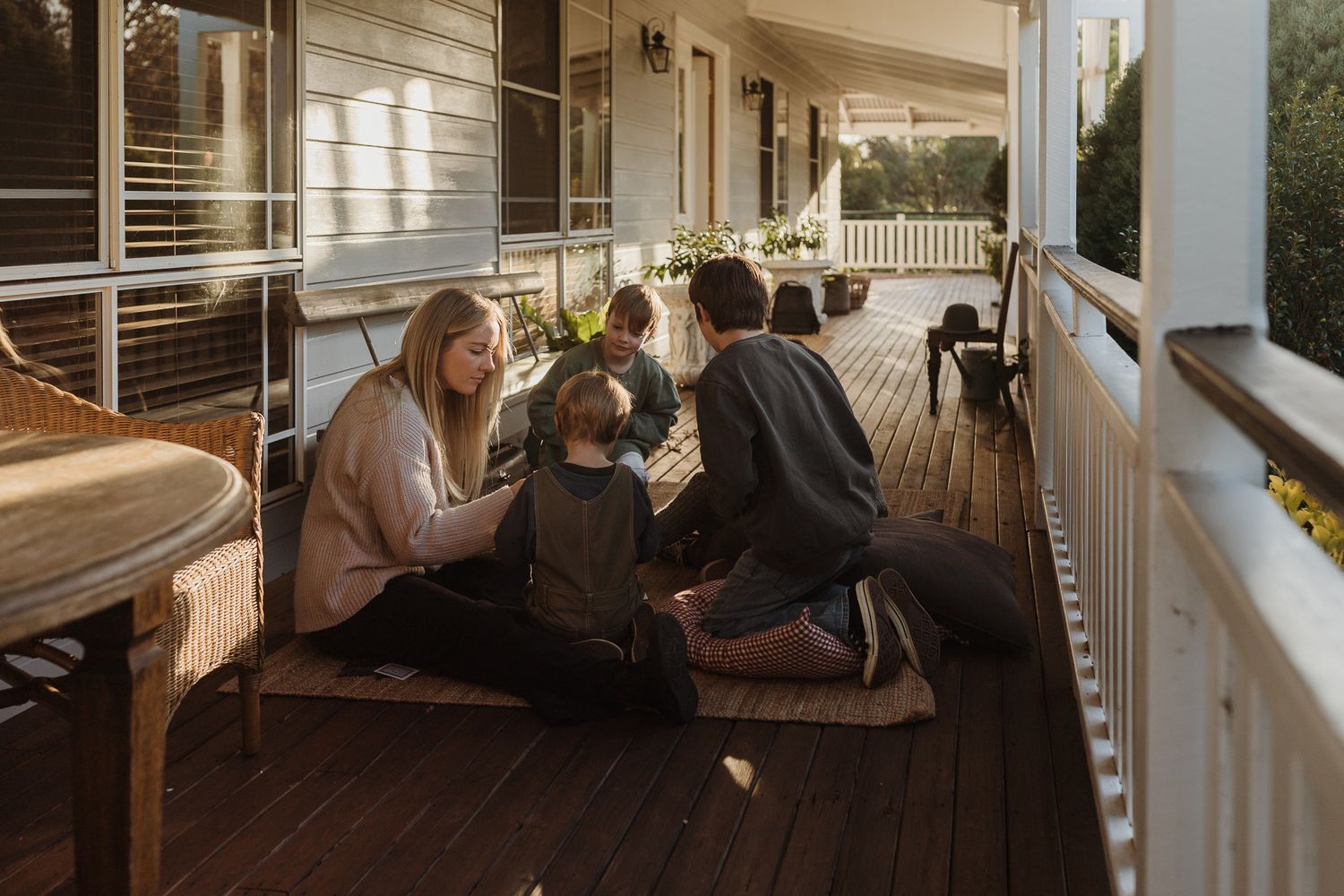 Family sitting on wide verandah playing cards with mum. 4 boys aged 4-12