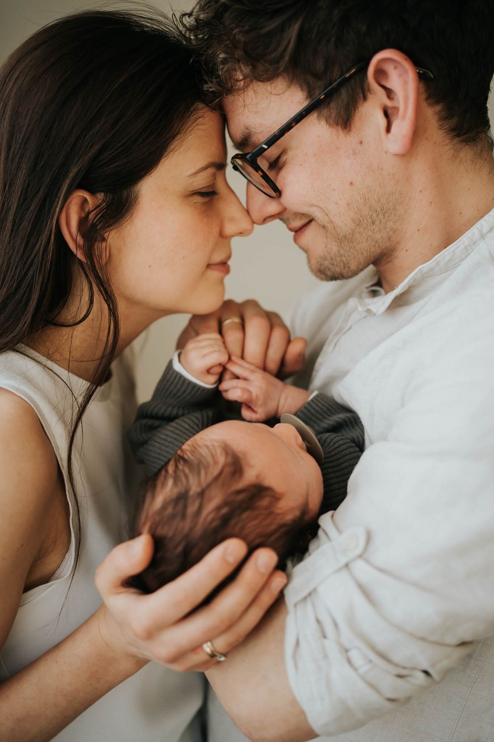 mama i tata stykają się czołami i nosami, tulą noworodka - sesja noworodkowa Kraków