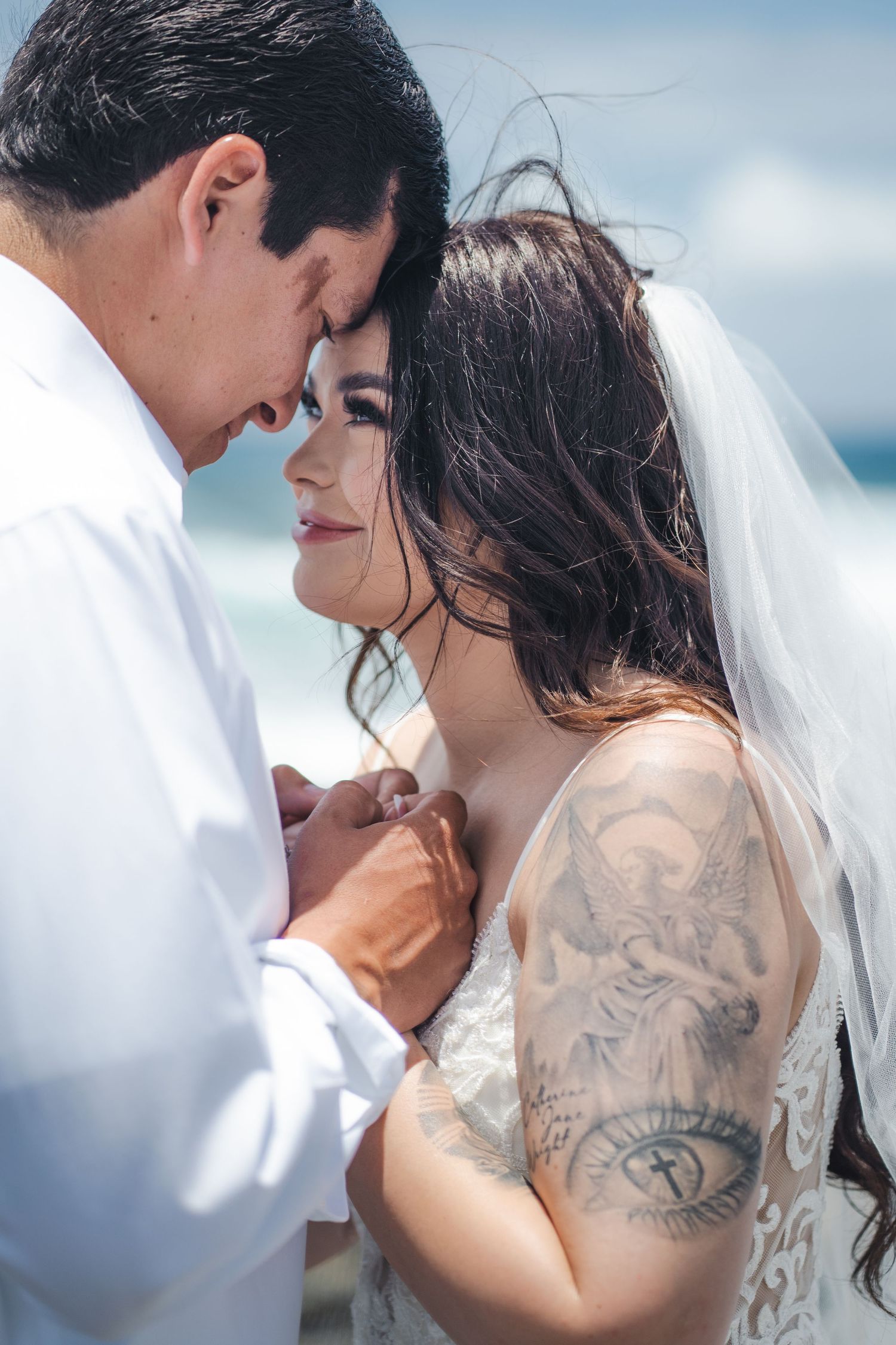 Intimate wedding portrait capturing tender moment with bride showing intricate arm tattoo.
