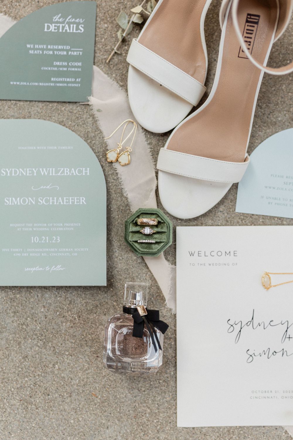 Wedding invitation suite in sage green with white shoes and perfume bottle.