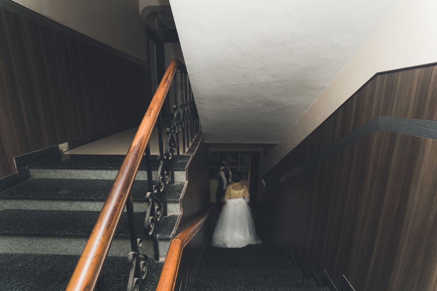 A wedding dress photographed at the bottom of a dark staircase with wooden railings.