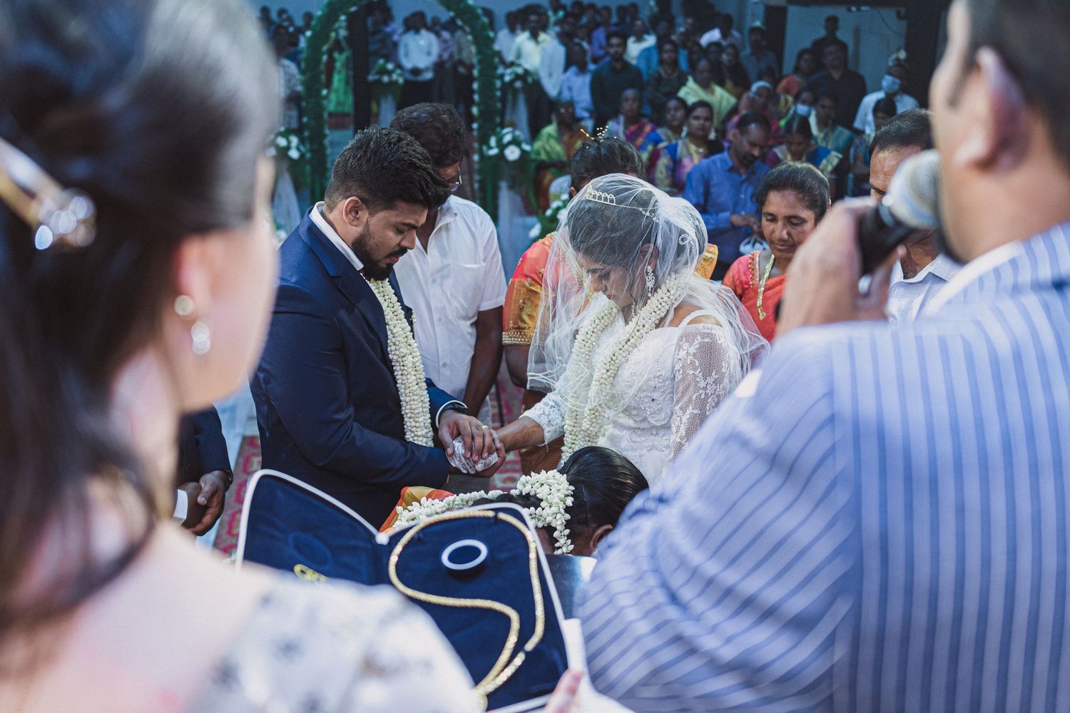 Traditional wedding ceremony with exchange of rings and white decor in background.