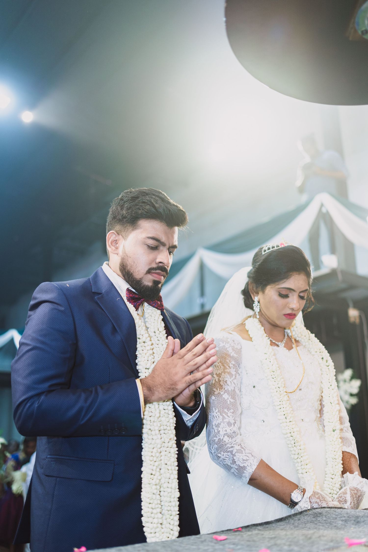 Couple at wedding altar wearing traditional white and navy attire during prayer.