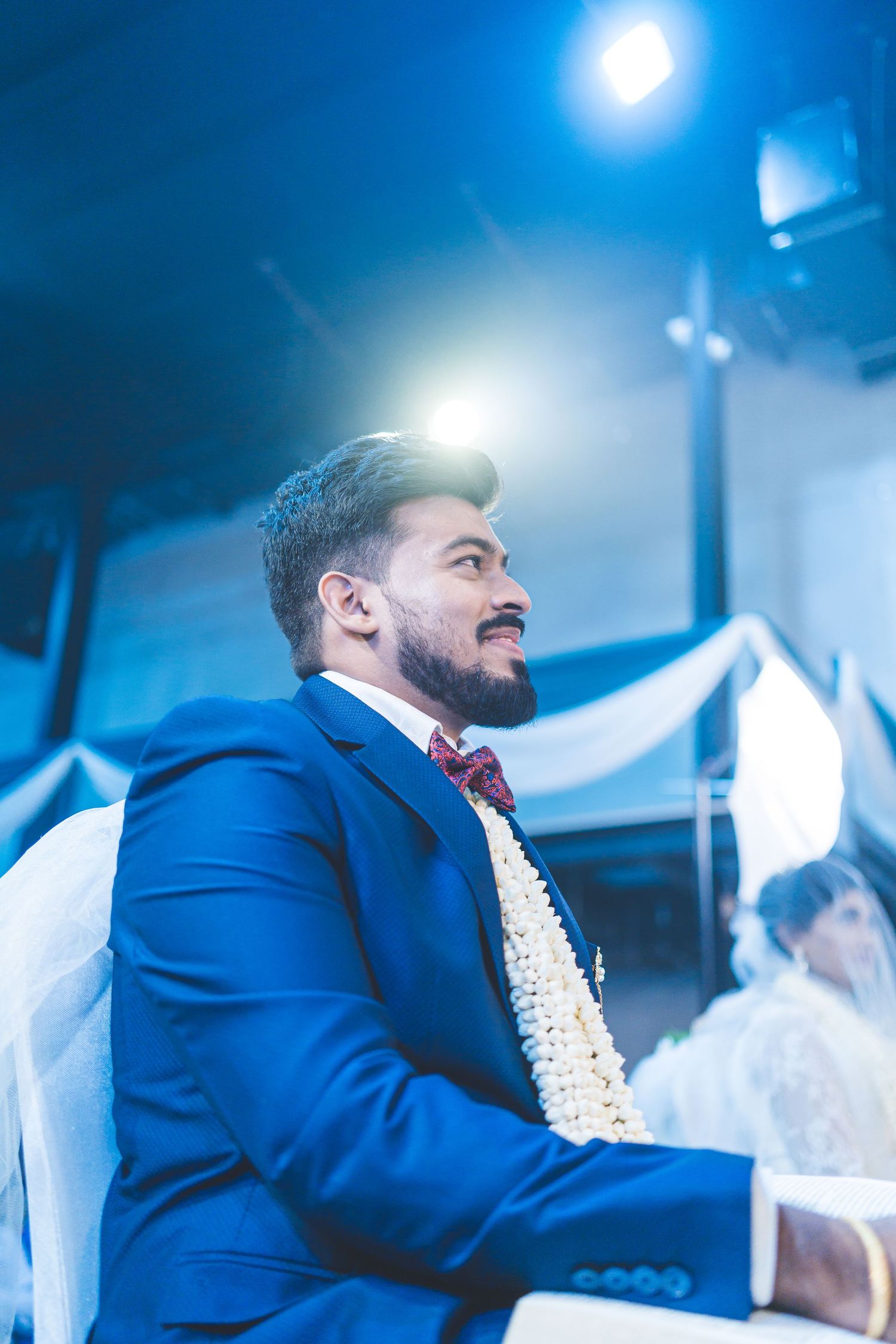 Person in royal blue suit and burgundy tie illuminated by dramatic blue lighting at formal event.
