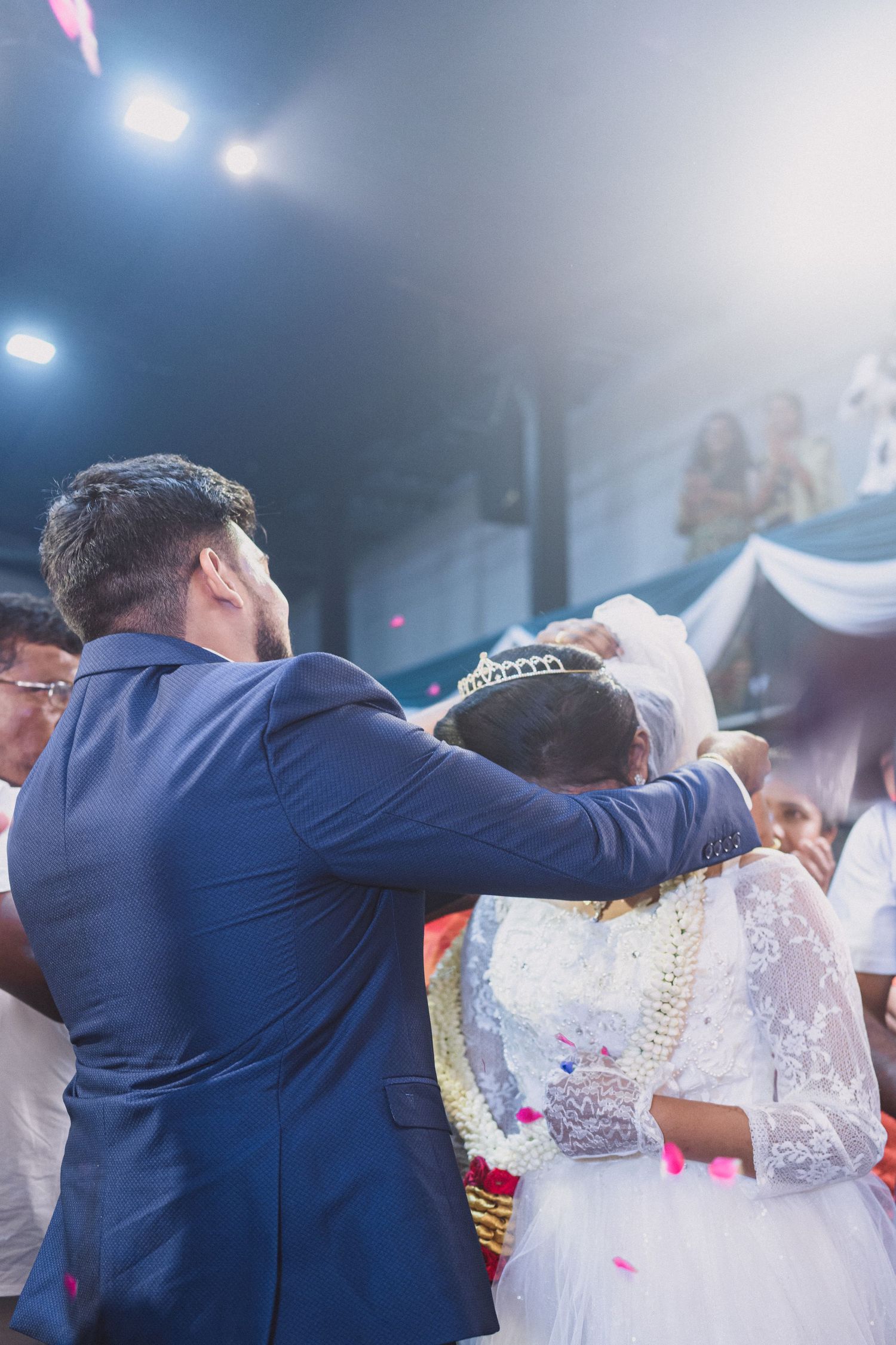 Emotional wedding moment captured during ring ceremony with confetti and blue lighting.