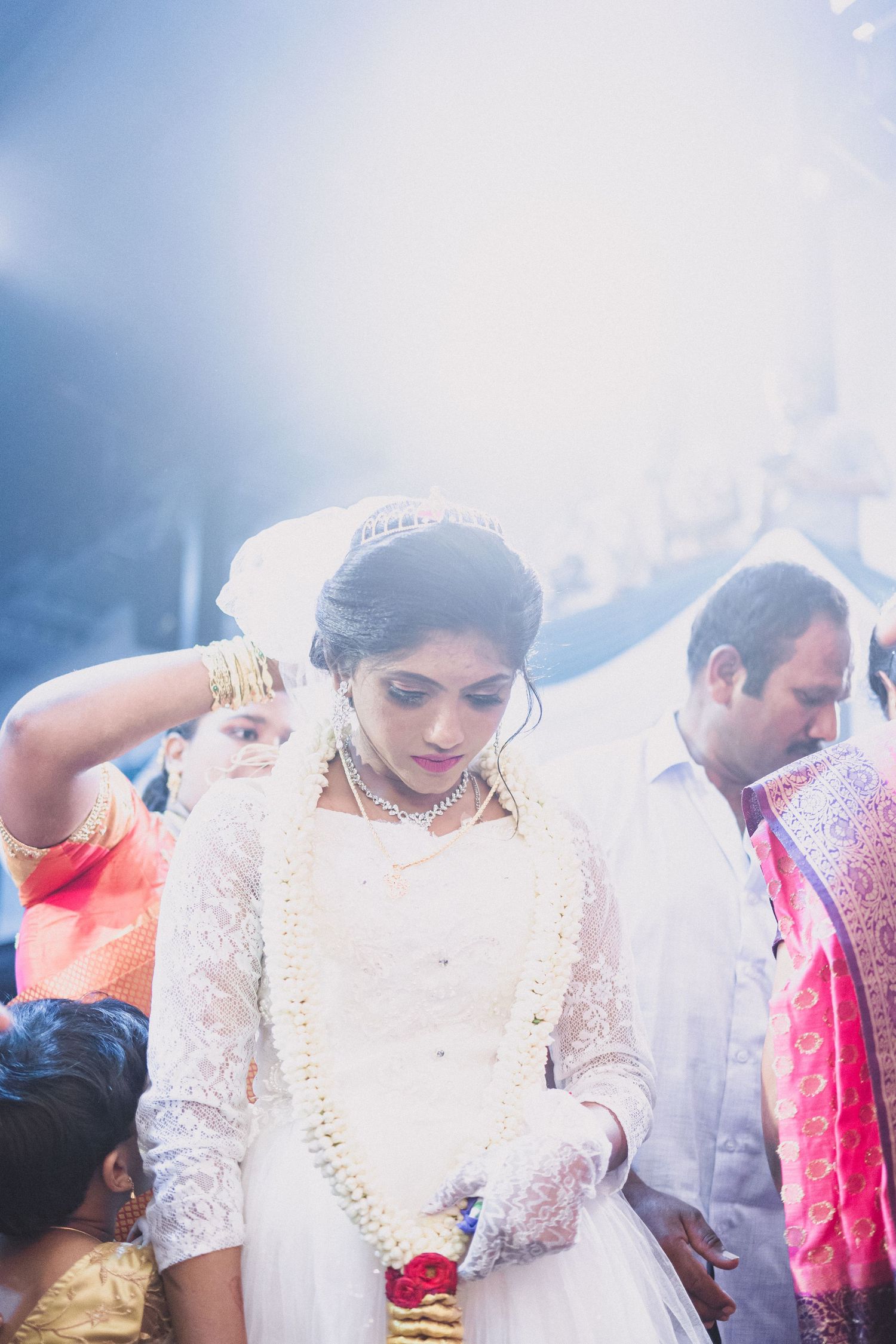 Bride adorned in elegant white dress with floral garland and lace details at wedding ceremony.