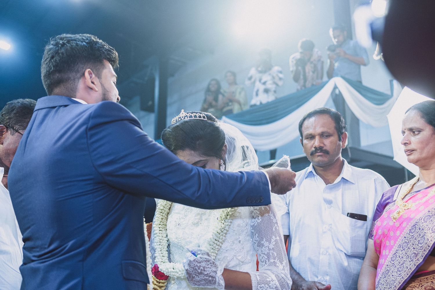 Wedding ceremony with guests watching as couple exchanges vows under blue and white decor.