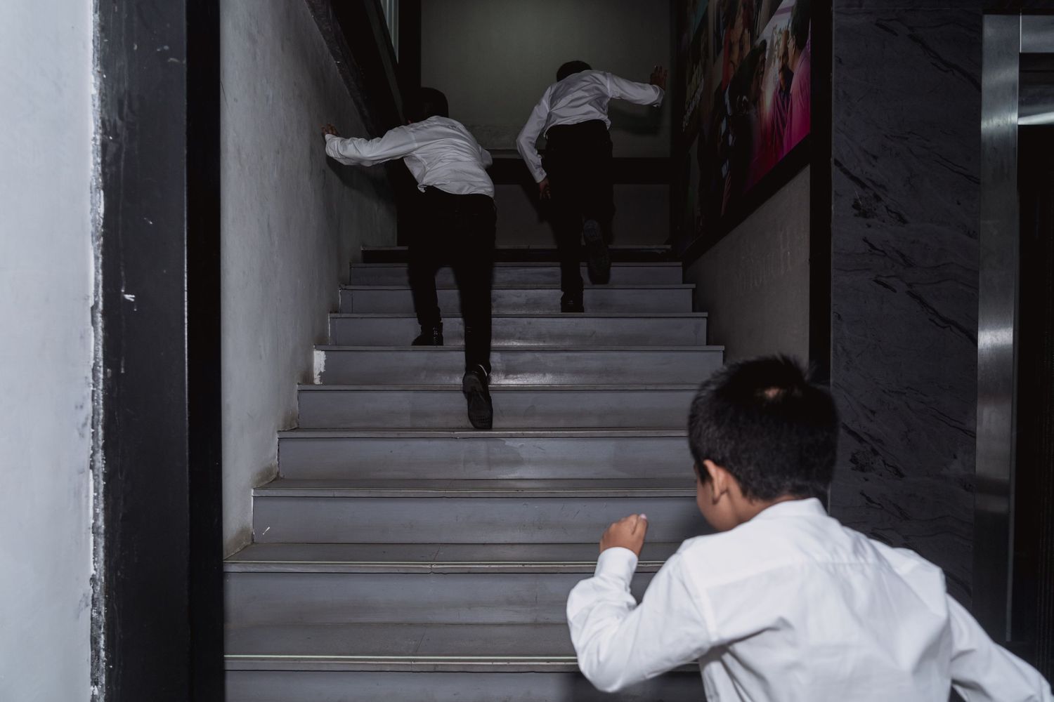 Children in white shirts run up grey stairs in a playful scene.