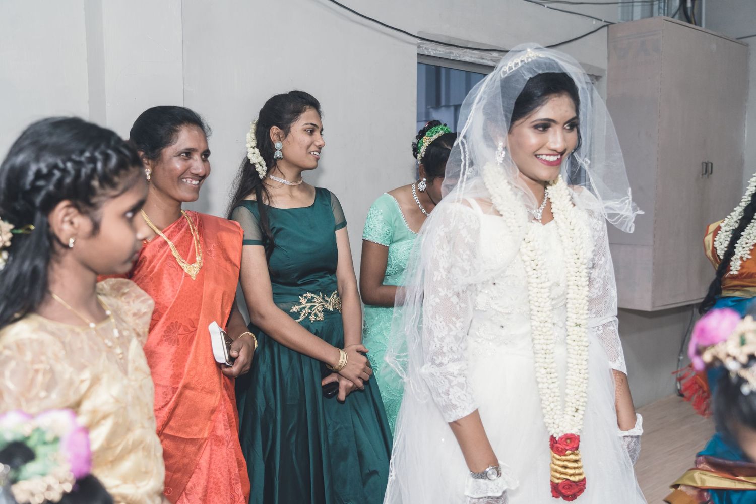 Bridesmaids in colorful traditional attire accompany a bride in white.