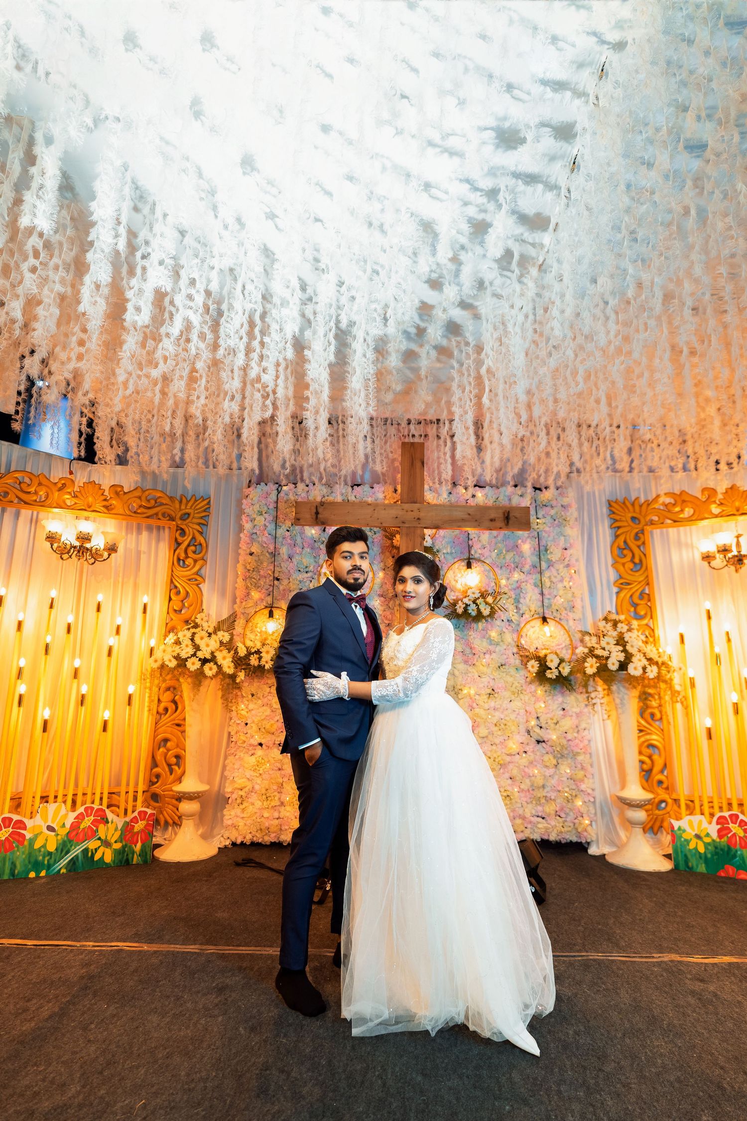 Wedding couple poses under a stunning white floral ceiling installation with golden lighting.