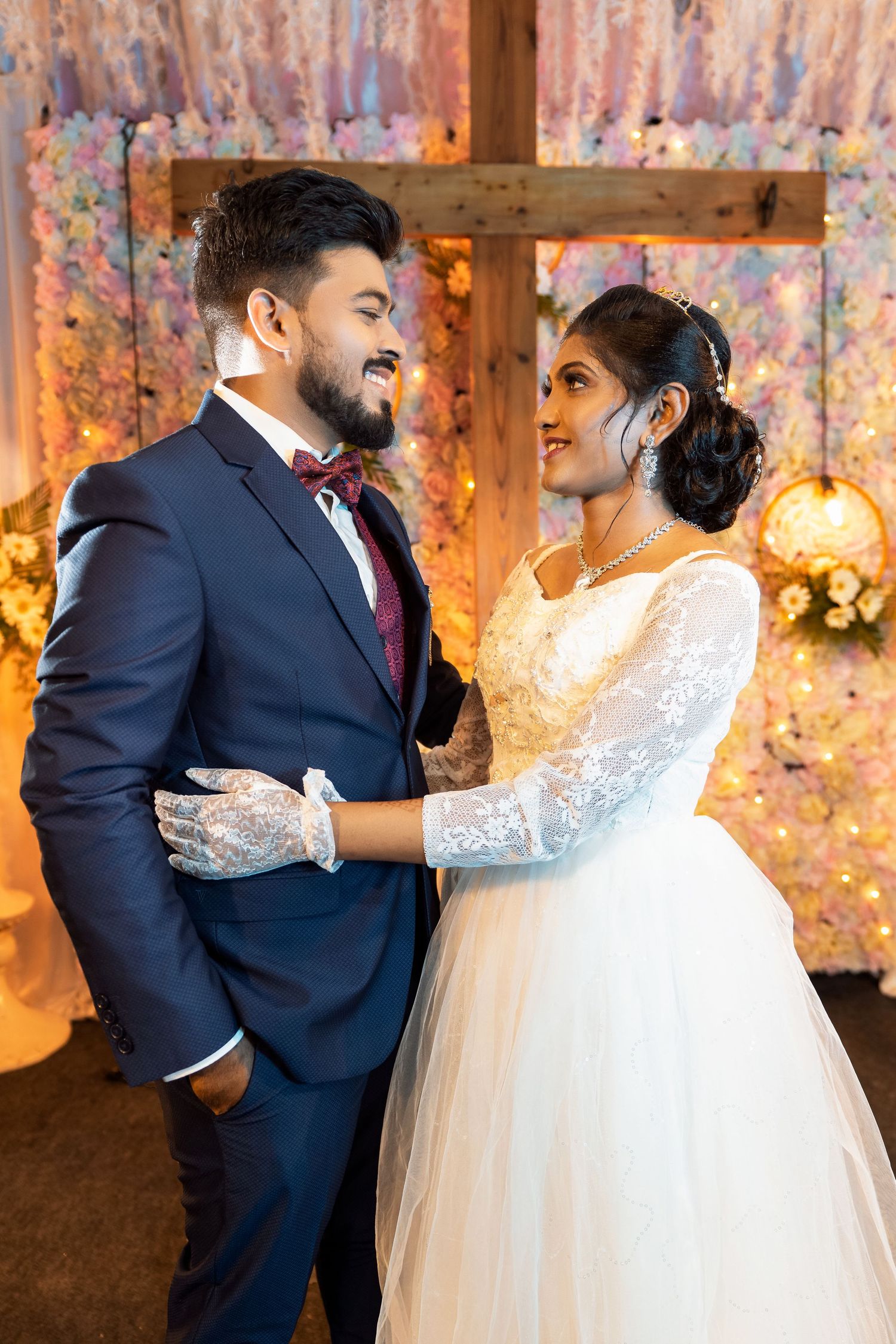Wedding couple shares a joyful moment under decorative lighting and floral backdrop.