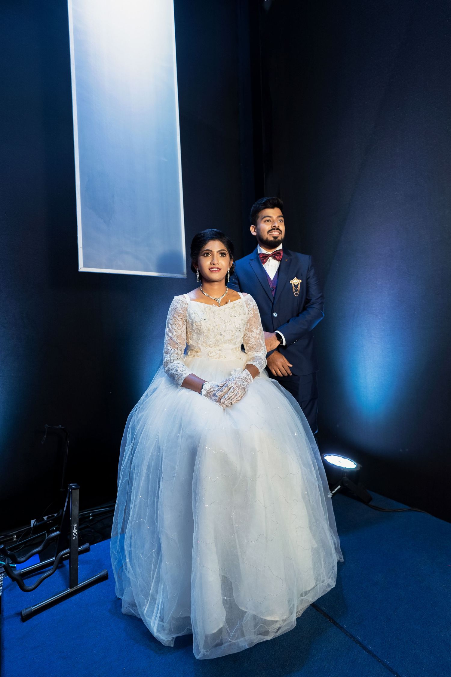Wedding couple poses dramatically under blue lighting against dark background.